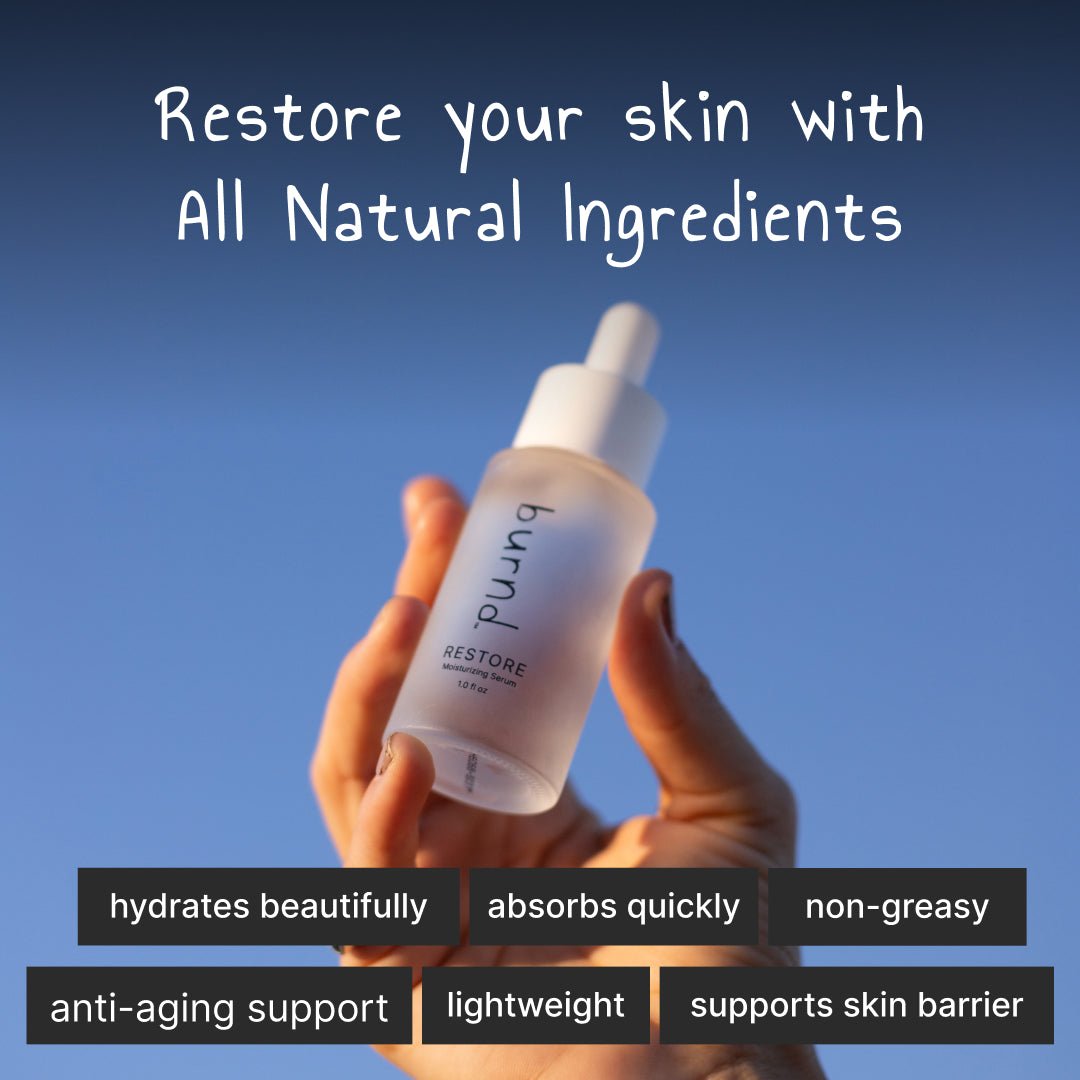 Hand holding a burnd Restore Serum bottle with text about natural ingredients and product benefits against a blue sky.