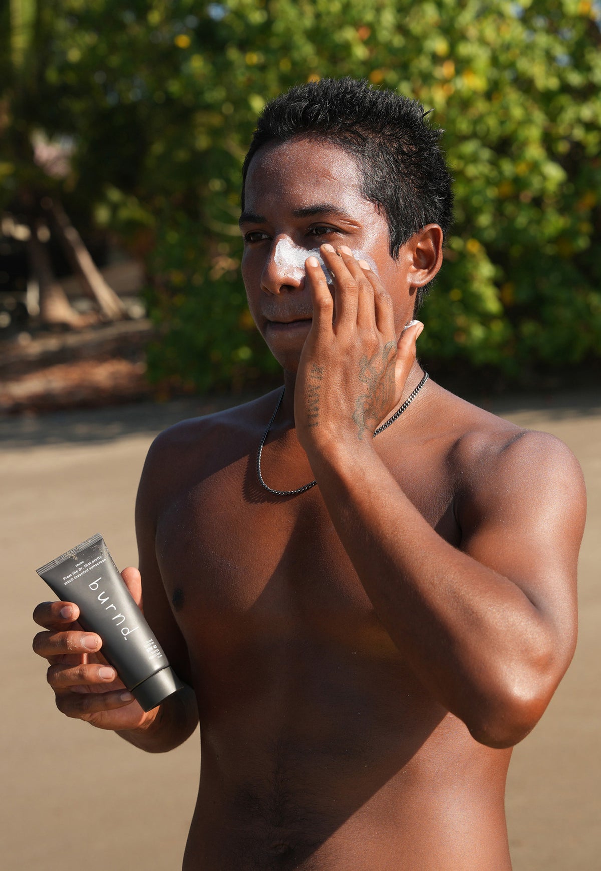 Man applying burnd sunscreen on a beach with a bottle of sunscreen in his hand