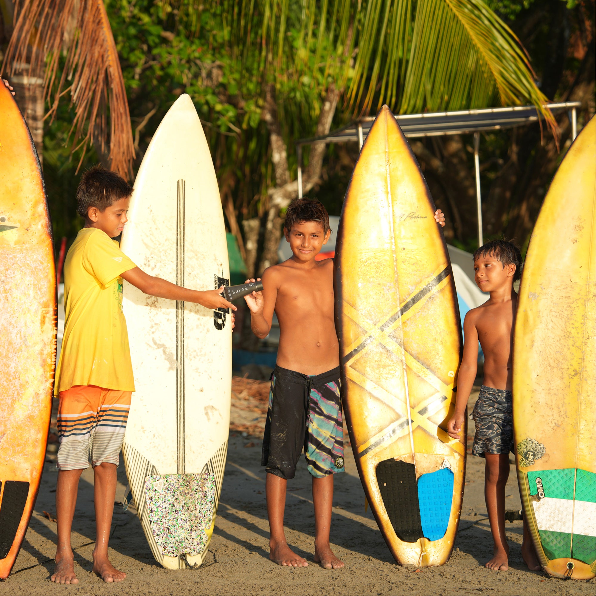 Three surfer kids sharing Burnd SPF41 sunscreen on the beach