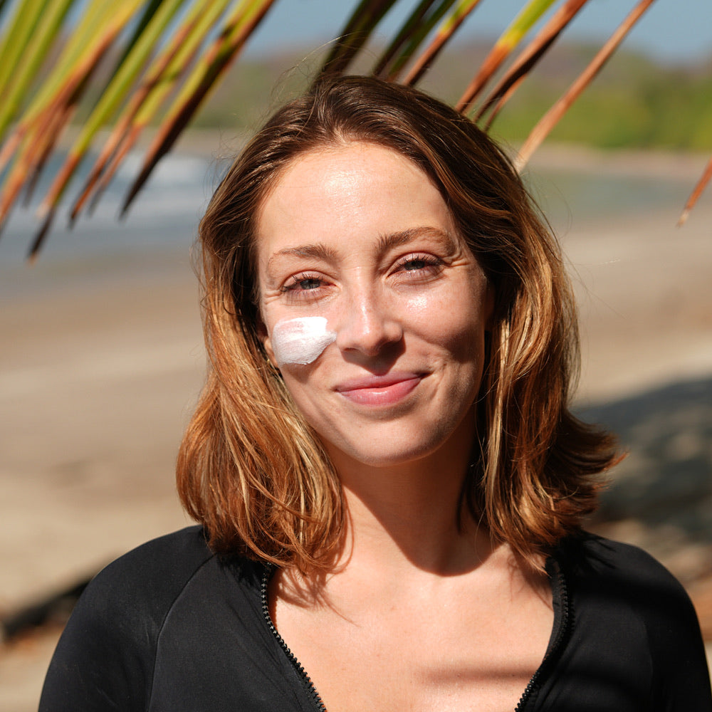 Woman with burnd SPF41 sunscreen on her face standing under a palm tree