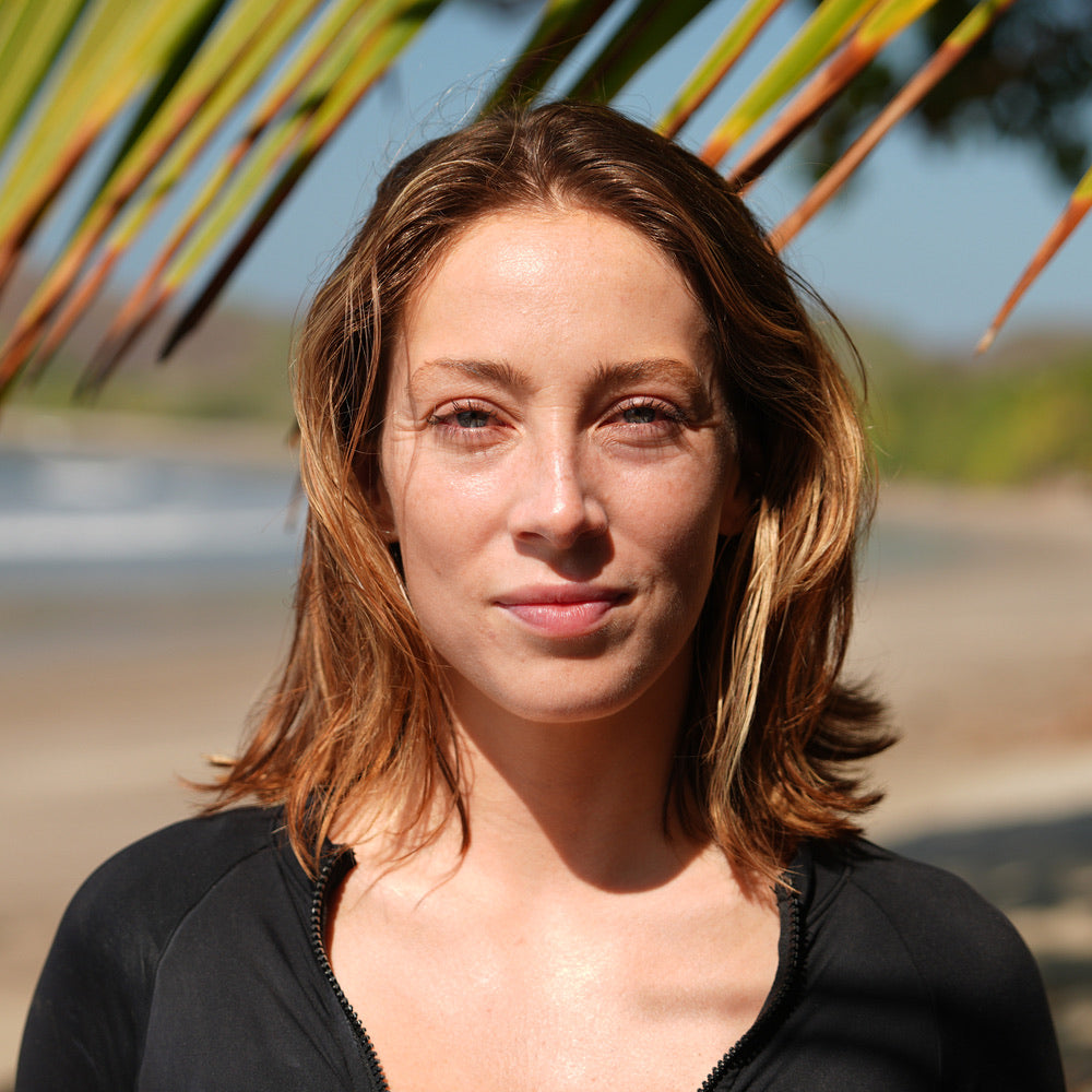 Woman standing outdoors without a white cast wearing SPF41 sunscreen with palm leaves in the background