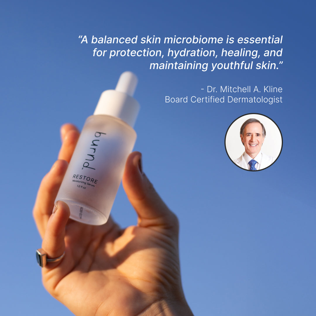 Hand holding a burnd restore hydrating skin serum with a quote from Dr. Mitchell A. Kline on a blue background saying:

"A balanced skin microbiome is essential for protection, hydration, healing, and maintaining youthful skin."