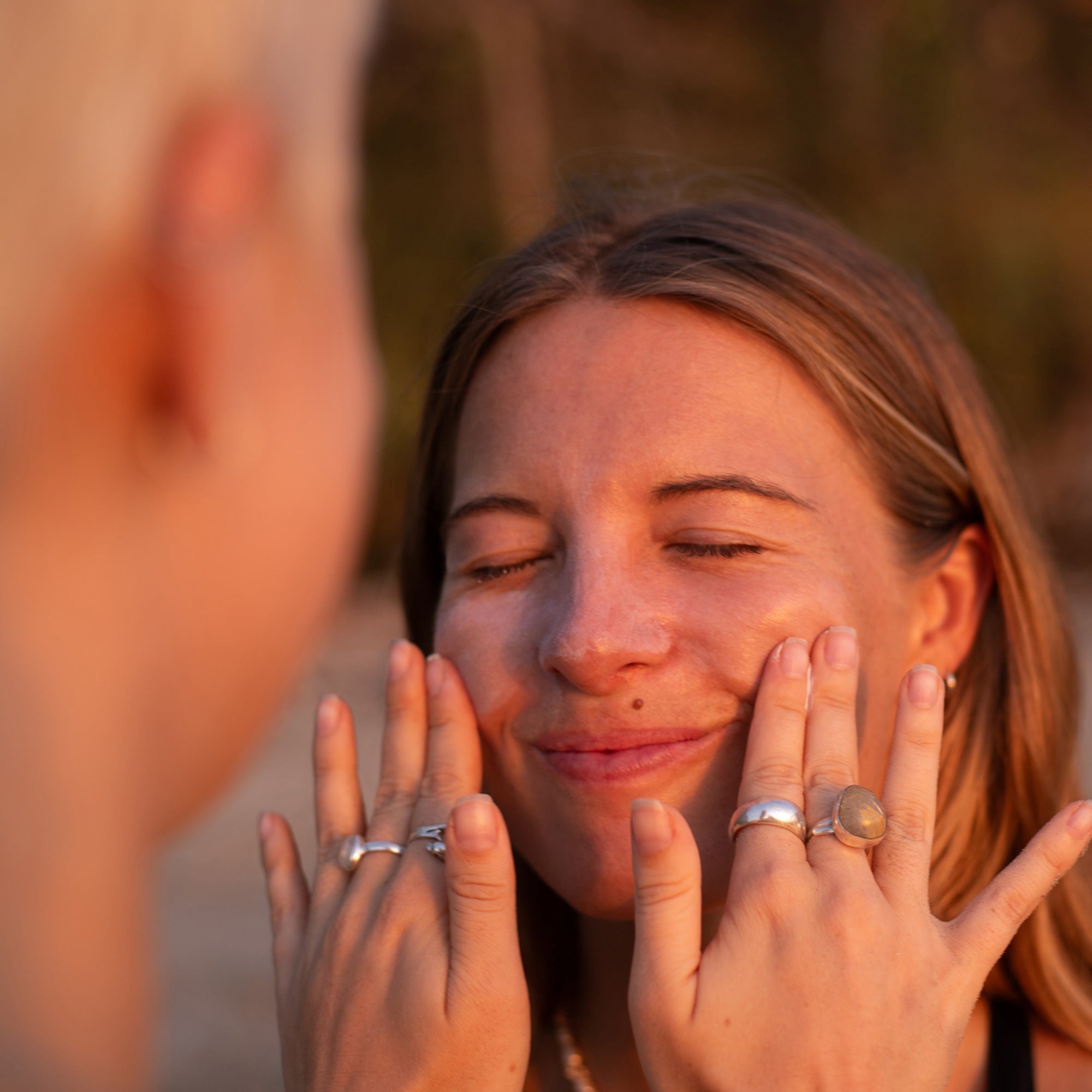 Woman having burnd sunscreen applied by a friend, showing how it will dry completely clear while still staying on