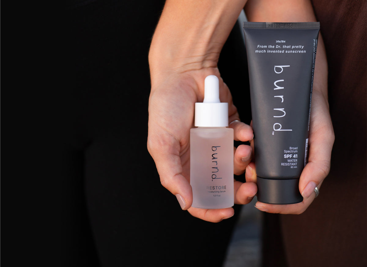 Two skincare products, the SPF41 and skin serum restore, from the brand 'burnd' held side by side against a dark background